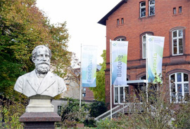Büste von Heinrich Eduard von Lade, Gründer der Königlichen Lehranstalt für Obst- und Weinbau zu Geisenheim; im Hintergrund ein Verwaltungsgebäude